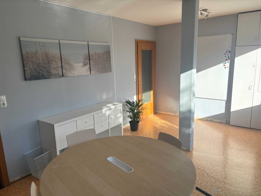 Besprechungsraum mit rundem Holztisch, weißem Sideboard und Whiteboard