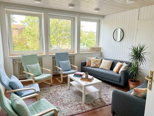 Chill-Ecke bei Justa+ mit hellblauen Sesseln, Sofa mit bunten Kissen und großen Fenstern